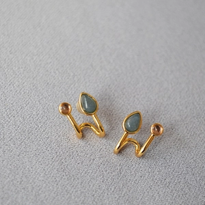 Vue macro de boucles d'oreilles dorées en U avec pierres vertes et roses en goutte