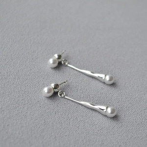 Minimalist silver long teardrop earrings with elegant pearls on gray textured surface