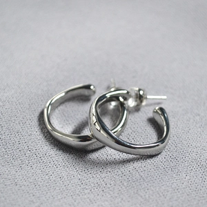 Macro shot of silver irregular hoop earrings with wavy texture on a grey fabric background