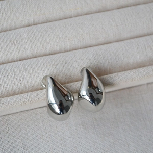 Macro shot of silver teardrop earrings with mirror finish on cream fabric stand