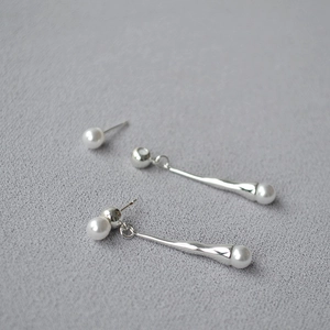 Detail view of silver drop earrings with black onyx and pearls on grey textured fabric