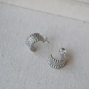 Close-up of silver C-shaped stud earrings featuring full pavé zircons and beaded edges