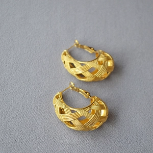 Detail of gold-plated woven mesh earrings showing intricate cross-textured hollow C-shape