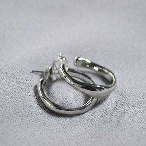 Detailed macro view of irregular wavy silver-plated hoop earrings with clear silicone plugs