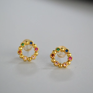 Détail de boucles d'oreilles couronne dorées avec pierres colorées et fermoirs silicone