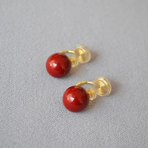 Boucles d'oreilles clips boules rouges avec crochets dorés sur fond en tissu gris