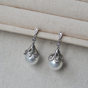 Detail of silver vintage pearl earrings with zircon flowers on beige jewelry display