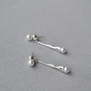 Minimalist long silver twist earrings with pearls on a textured grey surface