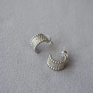 Macro detail of silver C-shaped stud earrings with pave-set cubic zirconia and beaded edges