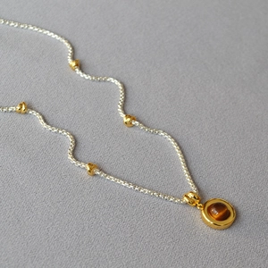 Detail of tiger eye stone pendant and silver beaded layered chain on grey texture
