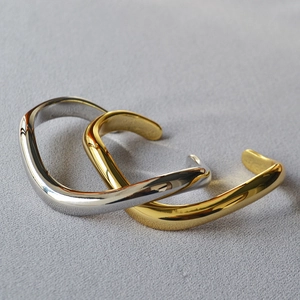 Detail view of irregular wavy open bangles in polished gold and silver metallic finishes