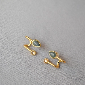 Détail de boucles d'oreilles dorées en forme de S avec pierre goutte sur tissu gris