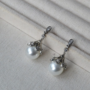 Vintage silver pearl drop earrings with sparkling zircon accents on beige textured fabric