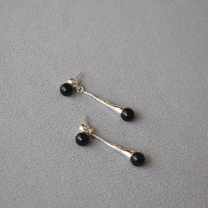 Minimalist silver long drop earrings with black onyx beads on textured grey background