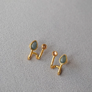 Détail de boucles d'oreilles dorées à double ligne avec pierres bleues et ambrées