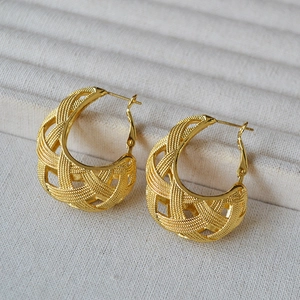 Detailed macro view of large gold hollow woven hoop earrings with intricate mesh texture