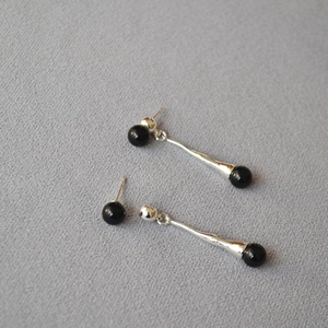 Macro detail of silver long teardrop earrings with black agate beads on gray fabric