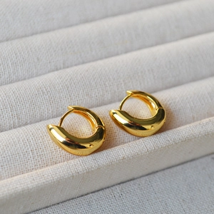 Close-up of polished gold-plated U-shaped huggie earrings in a minimalist jewelry box