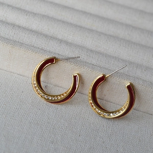 Close-up of C-shaped gold earrings with dark red enamel and sparkling zircons