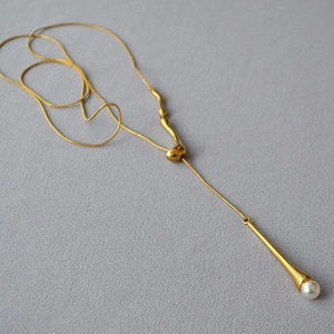 Vue détaillée du collier long doré avec des accents métalliques irréguliers et une perle