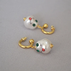 Macro shot of gold brass earrings featuring white pearls with green gem eyes and a smiley face