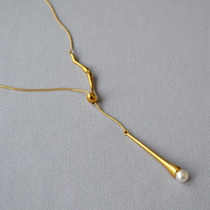Détail d'un long collier doré avec pendentif goutte et perle élégante en gros plan