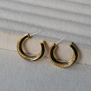 Detail of C-shaped gold-plated hoop earrings with black enamel and white zircons