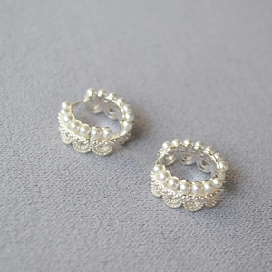 Détail de boucles d'oreilles couronne en dentelle avec perles blanches sur laiton doré