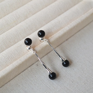 Macro view of long silver teardrop earrings with double black onyx beads on textile tray