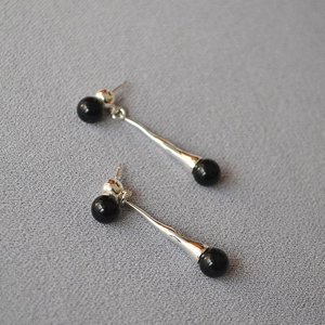 Macro detail of silver drop earrings with sleek black agate beads on textured fabric