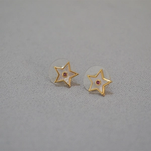Détail macro de boucles d'oreilles étoiles dorées avec incrustation blanche et gemme rouge