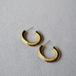 Detailed close-up of C-shaped gold-plated earrings with black enamel and zircon stones