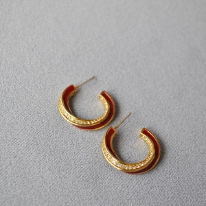 Detailed macro view of gold-plated C-shaped earrings with red enamel and pavé zircon stones