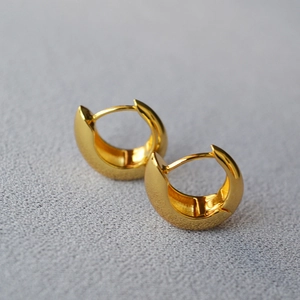 Macro view of polished gold plated thick hoop earrings on a grey textured fabric
