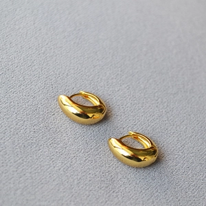 Close-up of polished gold-plated asymmetric hoop earrings on a grey textured surface