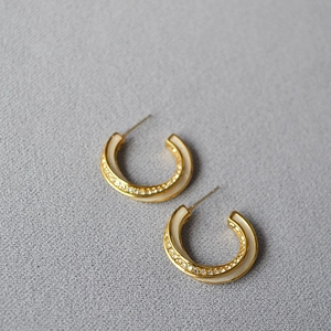 Macro detail of gold-plated Mobius hoop earrings with white enamel and pavé zircons