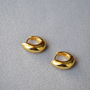 Detail view of gold-plated chunky huggie hoop earrings with polished mirror finish