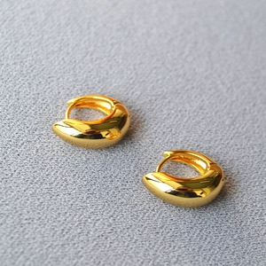 Macro shot of polished gold-plated asymmetric teardrop huggie earrings in detail