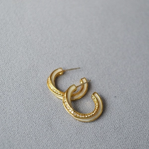 Detail of C-shaped gold plated earrings with white enamel and sparkling zircon accents