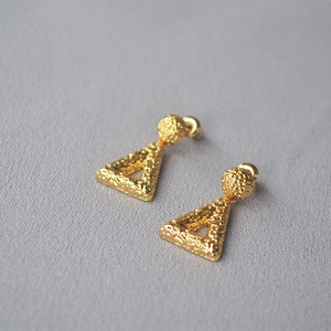 Macro view of gold-plated brass earrings with hammered texture and geometric hollow design