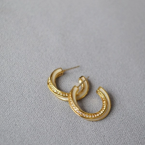 Close-up of gold-plated C-shaped earrings with white enamel and sparkling zircons