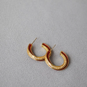 Detailed close-up of C-shaped gold earrings with red enamel and pavé-set crystals