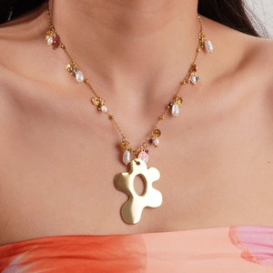 Gros plan d'un collier doré avec perles, visage souriant rose et pendentif fleur