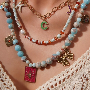 Détail d'un collier doré multicouche avec perles bleues, papillon et pendentifs