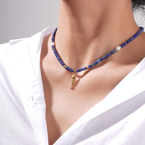 Collier en lapis-lazuli et perles avec pendentif poisson doré sur chemise blanche