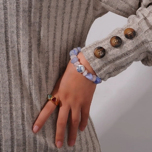 Bracelet en perles d'agate naturelle et bague dorée à deux pierres sur pull en maille gris