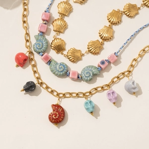 Layered gold chain necklaces with colorful skull charms and seashell bead pendants