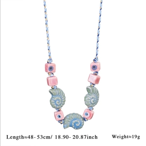 Detail of seashell necklace with blue woven cord, pink evil eye beads and green pendants