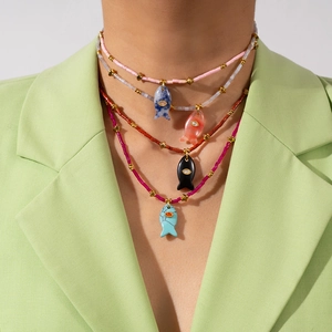 Layered colorful bead necklaces with synthetic stone fish pendants on a stylish model