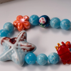 Ocean theme necklace with blue beads, sea star and crab charms on white background